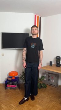 Svart grafisk t-shirt med en färgglad design, kombinerad med mörka vida jeans och mörka loafers med vita strumpor.