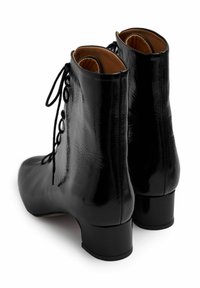 Černé kotníkové boty z lesklé lakované kůže s nízkým blokovým podpatkem, se šněrováním a hladkou texturou. Vnitřek vyplněný béžovou látkou.