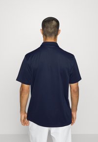 Polo bleu marine en tissu lisse, doté d'un col classique et de manches courtes, avec une coupe décontractée et des détails subtils de coutures au dos.
