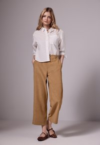 Valkoinen nappipaita, jossa on rintatasku, yhdistetty korkeavyötäröisiin, vaaleanruskeisiin leveälahkeisiin housuihin ja ruskeisiin leopardikuosisiksi lohkoilijakenkiin.