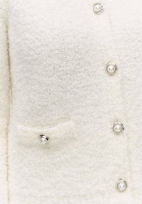 Witte textuur cardigan met een zachte, donzige stof. Voorzien van zilverkleurige knopen met parelaccenten en een klein voorvakje.