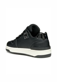 Sneaker nera con pelle liscia e dettagli in vernice. Presenta un profilo basso, una cinturino in velcro e una suola in gomma testurizzata.