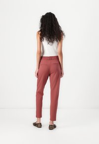 Roze gekleurde broeken met een relaxte pasvorm, elastische tailleband en twee achterzakken; gecombineerd met panterprint ballerina's, zicht vanuit de achterkant.