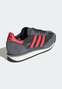 Zapatilla de ante gris y negra con acentos de rayas rojas, suela acolchada, cierre de cordones, talón texturizado y marca dorada "adidas SL '72."
