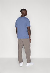 Tricou din bumbac albastru cu mâneci scurte, asortat cu pantaloni cargo bej. Adidași albi completează ținuta. Afișat din spate.