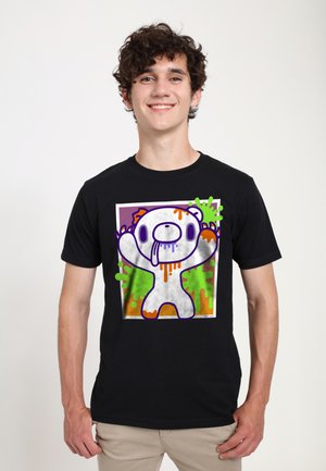 Smilende ung mand iført en sort T-shirt med farverigt graffiti-stil tegneserie bjørn design med orange og grønne malingssprøjt.