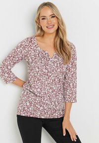 Kukkakuvioinen pusero 3/4-hihalla viininpunaisessa kankaassa, jossa on valkoisia kukkakuvioita ja V-pääntie, jossa on rypytystä.