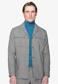 Jasnoszara kurtka w wzór houndstooth z frontowymi kieszeniami, kołnierzykiem typu lapel i zapięciem na guziki, nałożona na turkusowy golf.