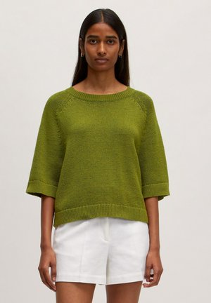 Pull en tricot vert à coupe ample, à manches courtes, avec un col et un ourlet côtelés ; associé à un short blanc. Tissu texturé d'un éclat subtil.