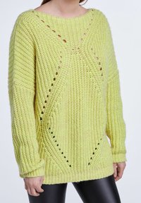Pull en maille vert clair à coupe ample, avec un large col, de grosses mailles et des motifs ajourés le long des côtés et des manches.