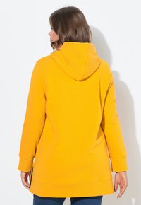 Felpa gialla con cappuccio e maniche lunghe, fianchi aperti all'orlo e un tessuto texture. La vista posteriore mostra un design semplice e liscio.
