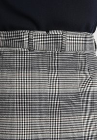 Schwarz-weiß kariertes Stoff mit einem strukturierten Bund, der verschiedene Muster wie Hahnentritt und Karomuster aufweist.