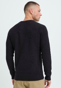 Dunkles Strickpullover mit strukturiertem Muster und Rundhalsausschnitt, mit langen Ärmeln und lockerer Passform, von hinten gezeigt.