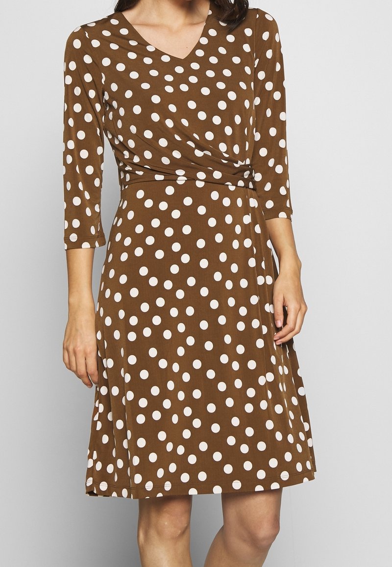 Robe marron à pois avec manches trois-quarts, col en V et taille cintrée, fabriquée en tissu doux orné de grands pois blancs.