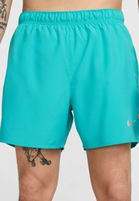 Turkoosi urheilushortsit, jotka on valmistettu kevyestä kankaasta ja joissa on joustava vyötärönauha sekä pieni hopeinen Nike-logo alhaalla oikeassa lahkeessa.