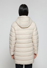 Abrigo tipo puffer en beige claro, con capucha, costuras horizontales y un diseño de longitud media. Material texturizado con un acabado suave.