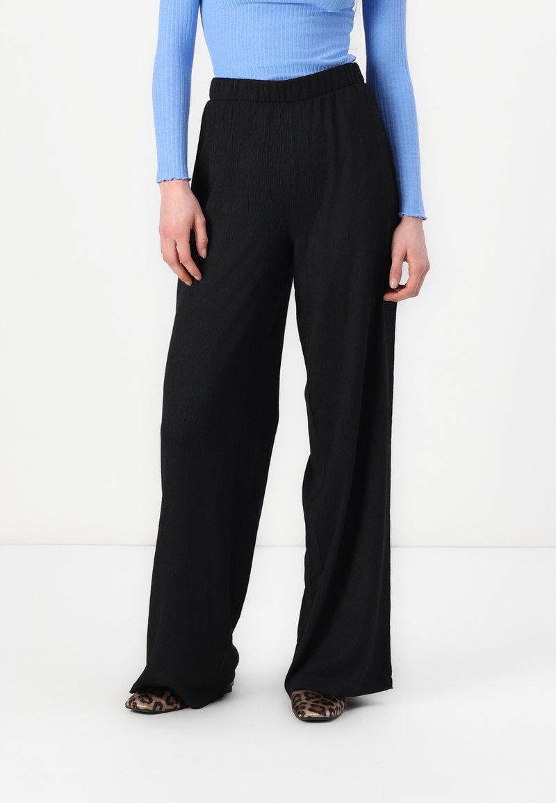 Black wide-legged pants with a textured finish, featuring an elastic waistband. Paired with a blue ribbed long-sleeve top and animal print shoes.