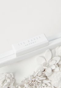 Clutch bianca in pelle con dettagli floreali in rilievo. Presenta un logo argento "Ted Baker London" e un design elegante e minimalista.