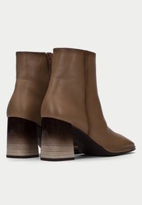Botas de tobillo de cuero marrón con punta afilada y un alto tacón cuadrado que presenta una textura en degradé. Cierre de cremallera lateral para facilitar el uso.