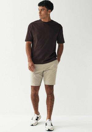Tricou maro cu guler rotund, pantaloni scurți bej și adidași albi cu accente negre. Croială casual, design simplu și texturi moi.