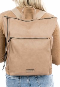 Zaino in pelle tan con tasca frontale con zip, texture liscia, maniglia superiore e spallacci regolabili. Presenta un'etichetta del marchio sul fondo.