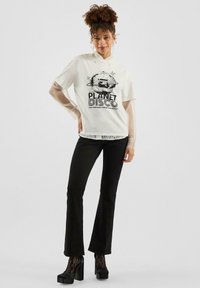 Witte t-shirt met "PLANET DISCO" graphic, doorzichtige mesh mouwen, gecombineerd met flared zwarte broek en platform schoenen met veters.