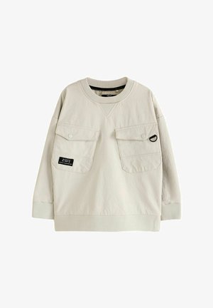 Helebeige dressipluus, pikkade varrukatega, kahe esiosa taskuga, ribaga kaeluse ja mansettidega ning sildiga vasakul taskul. Sile kangastekstiil.