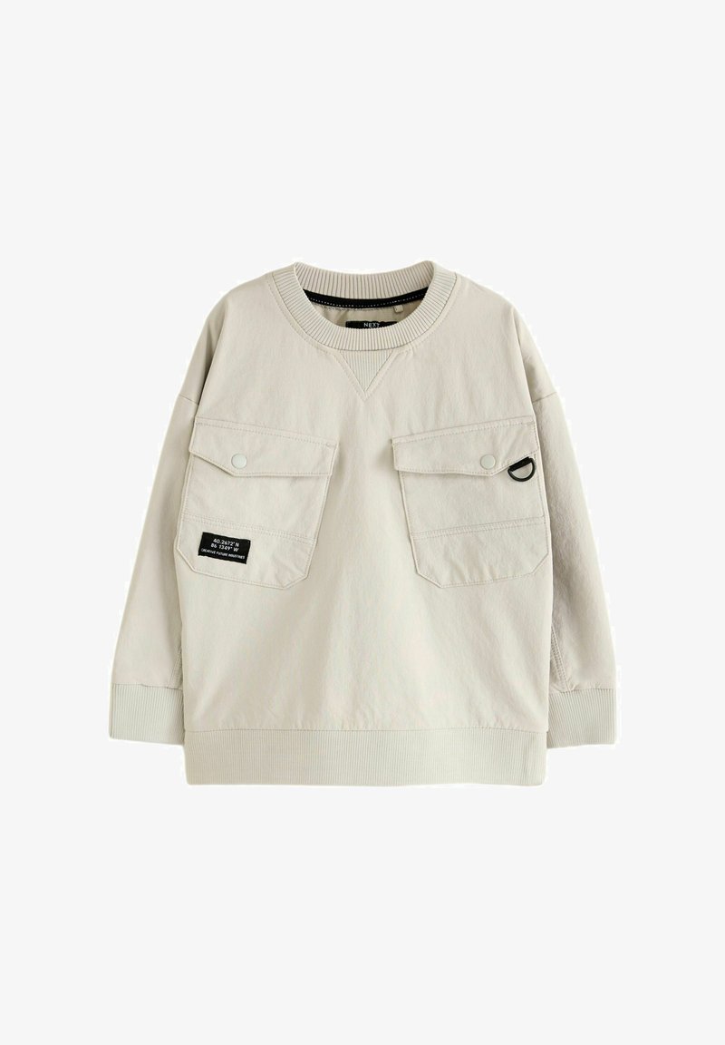 Sweat-shirt beige clair aux manches longues, deux poches avant, col et poignets côtelés, et une étiquette sur la poche gauche. Texture de tissu lisse.