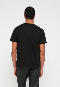 Μαύρο κοντομάνικο μπλουζάκι με λαιμόκοψη, βαμβακερό υλικό και μικρό ετικέτα στο τελείωμα, εμφανιζόμενο από πίσω.