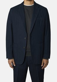 Mörkblå kavaj i strukturerad tyg, med två knappar, två framfickor och slagkrage, bärs över en mörkgrå tröja.