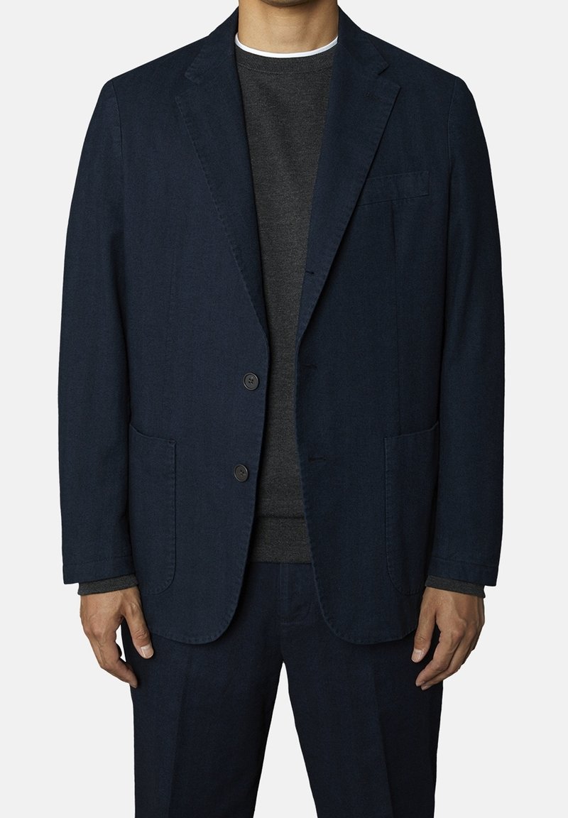 Mörkblå kavaj i strukturerad tyg, med två knappar, två framfickor och slagkrage, bärs över en mörkgrå tröja.