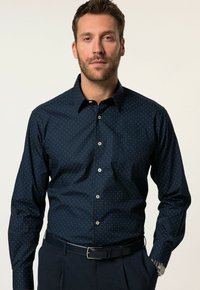 Camicia blu navy con bottoni, a pois bianchi, maniche lunghe e colletto standard. Presenta bottoni a contrasto e una tasca sul petto.