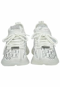 Zapatillas deportivas blancas con un upper de tela texturizada que presenta detalles plateados, cordones y patrones en los lados. Suelas gruesas y blancas.