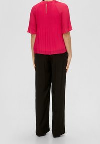 Blusa rosa con pliegues y mangas cortas, detalle de ojal en la espalda, combinada con pantalones negros de pierna ancha, textura de tejido suave.