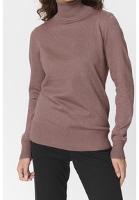 Bruine ribbel turtleneck trui van een zachte breimateriaal, met een aansluitende stijl en een brede ribbelzoom, gedragen met zwarte broek.