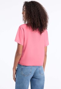 Růžové tričko s krátkými rukávy, kulatým výstřihem a volným střihem, spárované se světle modrými džínami. Látka vypadá hladce a jemně.