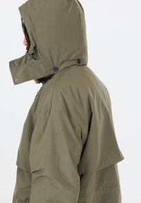 Olivgrön, vattentät jacka med huva. Har en avslappnad passform, tryckknappar och en slät, matt textur.