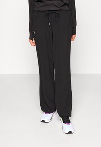 Svarta träningsbyxor med lös passform och elastisk midja. Inkluderar sidofickor och en liten logotypdetalj. Bärs med vita och lila sneakers.