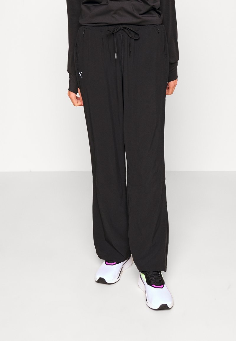Svarta träningsbyxor med lös passform och elastisk midja. Inkluderar sidofickor och en liten logotypdetalj. Bärs med vita och lila sneakers.