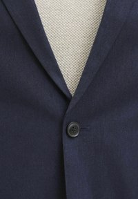 Blazer marine avec un col cranté, fermeture à un bouton noir et texture lisse sur un fond clair.