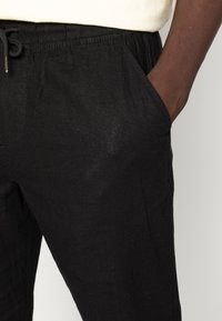 Zwarte linnen broek met een elastische tailleband en trekkoord. Bevat zijzakken, een ontspannen pasvorm en een zachte, gestructureerde stof.