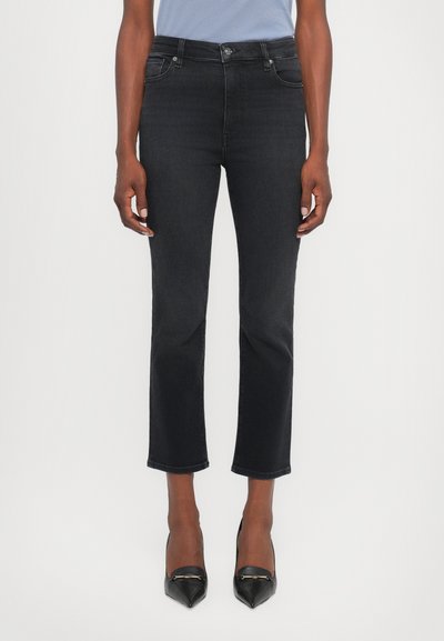 Jeans in denim neri con una vestibilità slim, vita media e orlo accorciato, abbinati a tacchi a punta neri. Texture liscia e minimalismo nei dettagli.