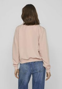 Light pink sweatshirt with a relaxed fit, ribbed cuffs, and hem, paired with blue high-waisted jeans, viewed from the back.