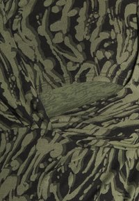 Olivgrön tyg med en strukturerad ribbad mönstring med svarta abstrakta former. Inkluderar en partiell urklippning vid midjan.
