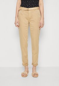 Beige chinos med avslappnad passform, uppvikta muddar och ett flätat ljusbrunt bälte. I kombination med platta, vävda sandaler med remdesign.