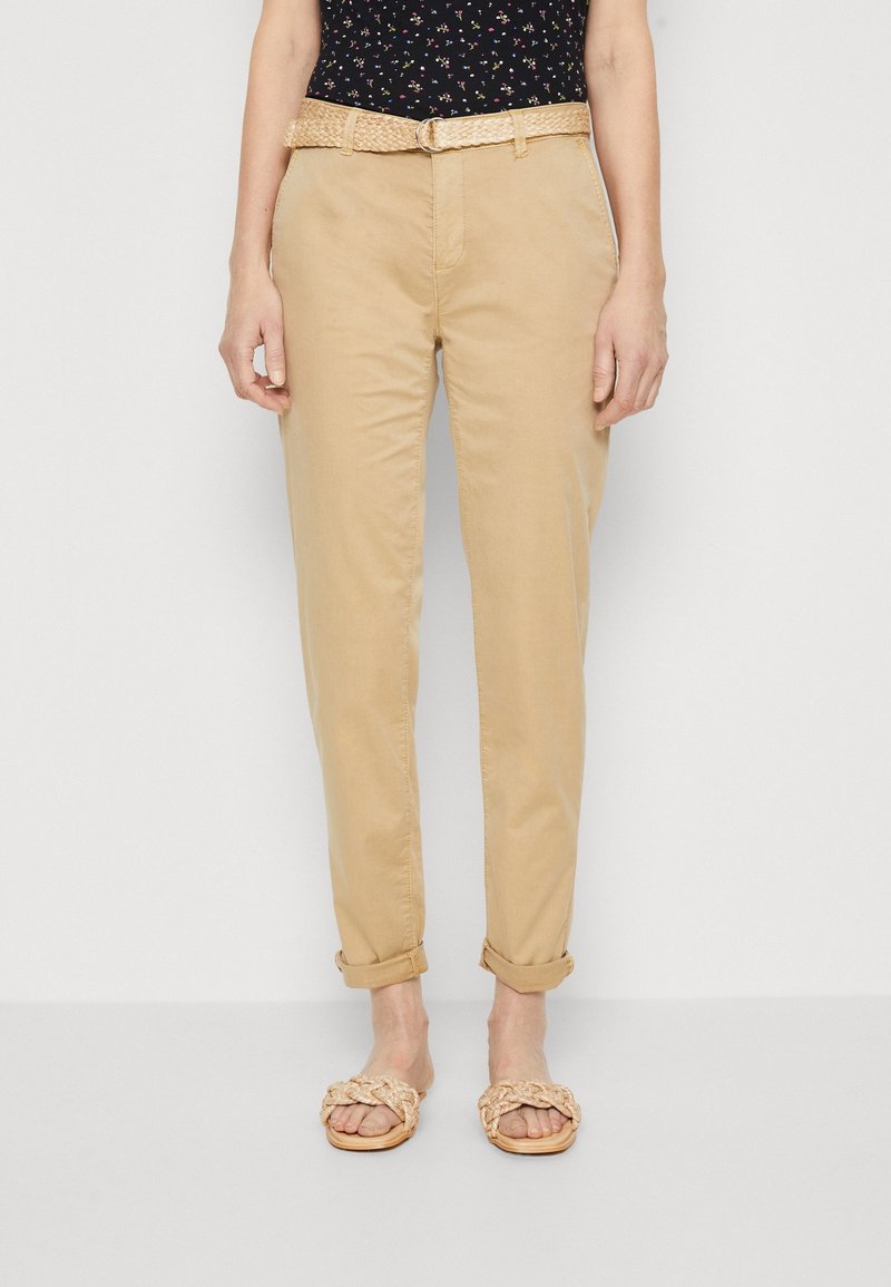 Beige chinos med avslappnad passform, uppvikta muddar och ett flätat ljusbrunt bälte. I kombination med platta, vävda sandaler med remdesign.