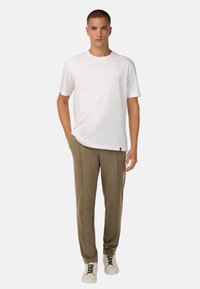 Balta trumpa rankovėmis marškinėliai derinami su alyvuogių spalvos siaurėjančiomis treniruočių kelnėmis ir smėlio spalvos sportbačiais. Apranga pasižymi laisvu siluetu ir minimalistiniu dizainu.