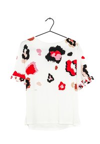 White short-sleeve blouse with abstract floral patterns in red, black, pink, and beige, hanging on a black hanger against a white background.