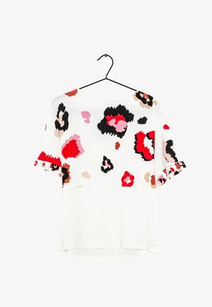 White short-sleeve blouse with abstract floral patterns in red, black, pink, and beige, hanging on a black hanger against a white background.