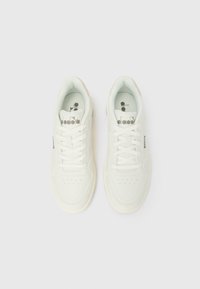 Poros baltų Diadora sportinių batų su raišteliais, perforuotomis priekinių dalių dalimis ir logotipu ant liežuvėlių, parodytos iš viršaus šviesiame fone.